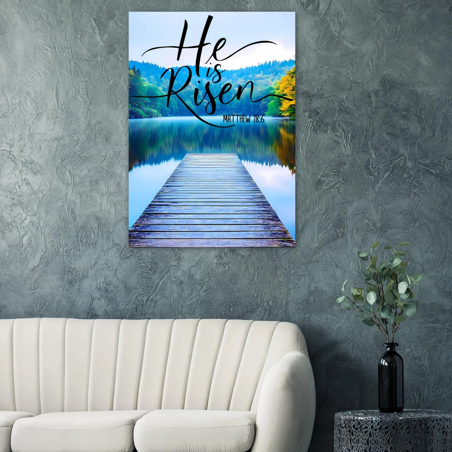 Canvas print with 'He is Risen' text over a dock scene on a wall above a sofa.