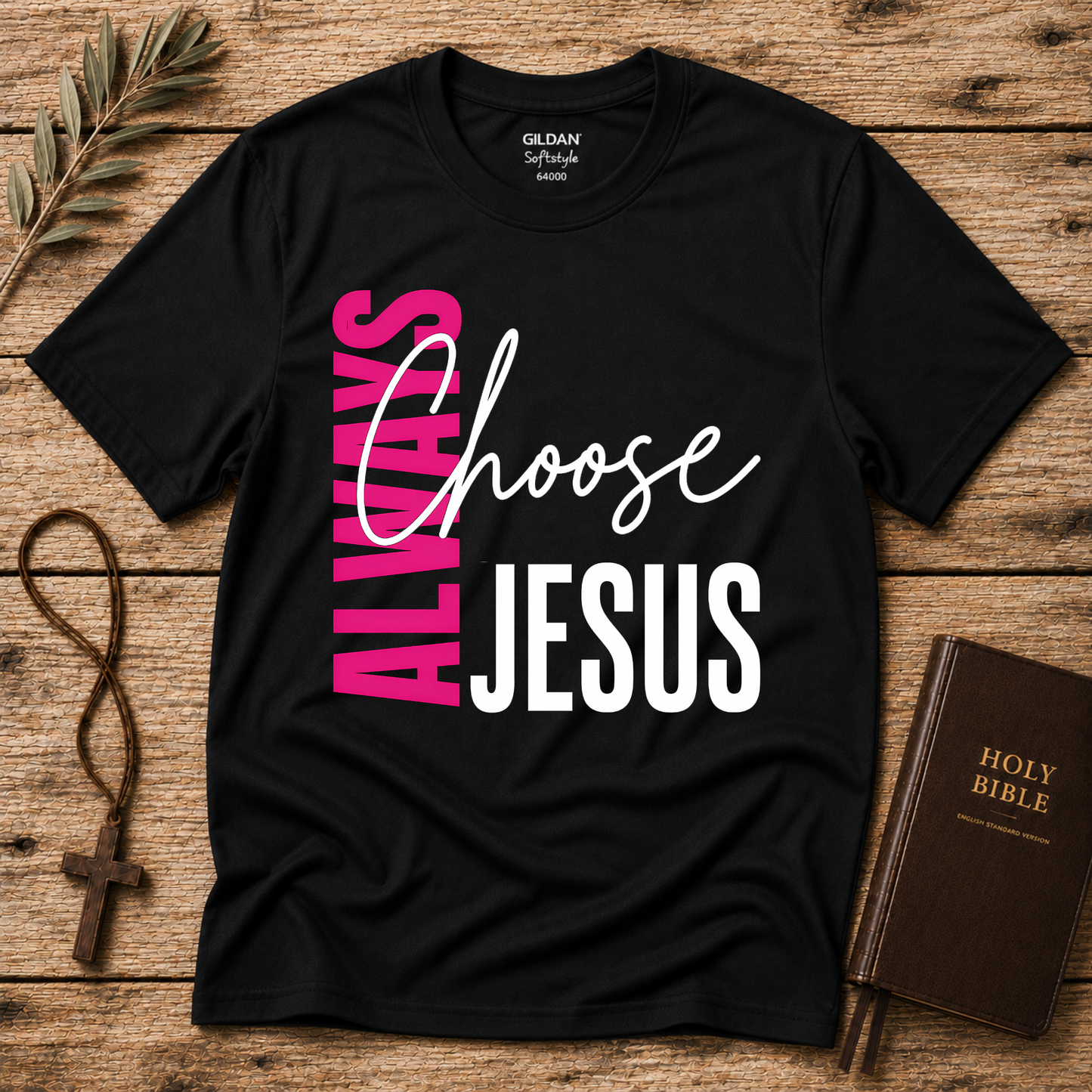 A black Gildan Short Sleeve t-shirt with a graphic reading 'ALWAYS Choose JESUS' in pink, white, and black, styled in a flat-lay on a rustic wooden background with a rosary, olive branch, and Holy Bible.
