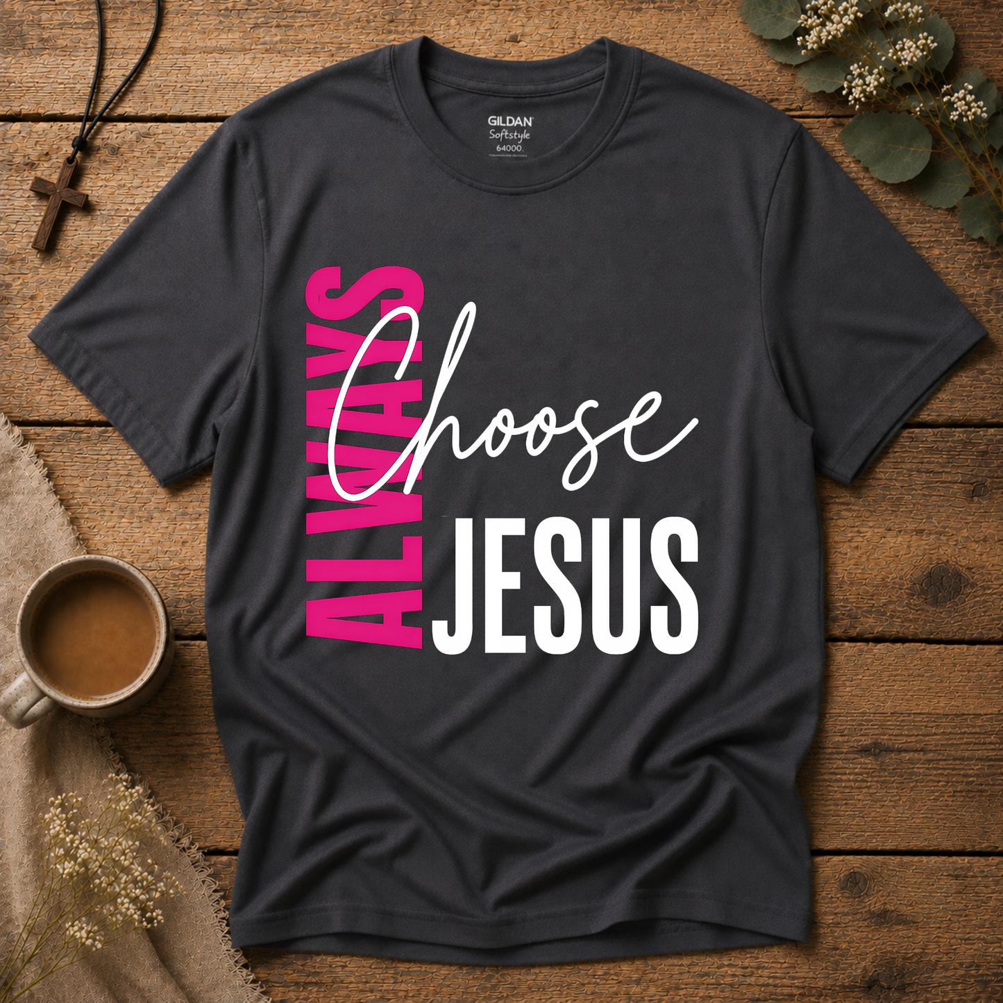 A dark charcoal gray Gildan t-shirt with a graphic reading 'ALWAYS Choose JESUS' in pink, white, and black, laid flat on a rustic wooden background with lifestyle props like a coffee mug, cross necklace, and dried flowers.