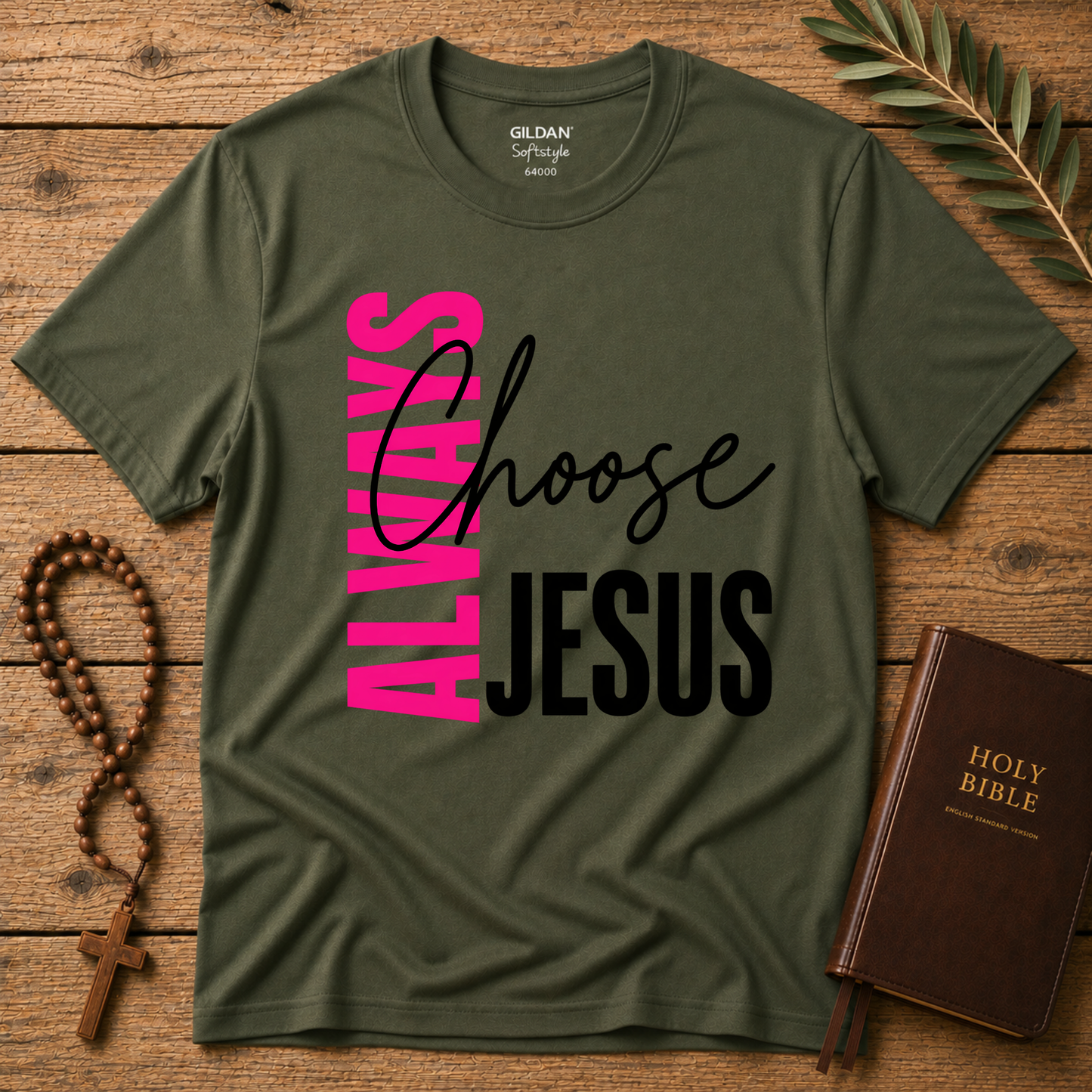 An olive green Gildan t-shirt with a graphic reading 'ALWAYS Choose JESUS' in pink and black, styled on a wooden background with a rosary and a Holy Bible.