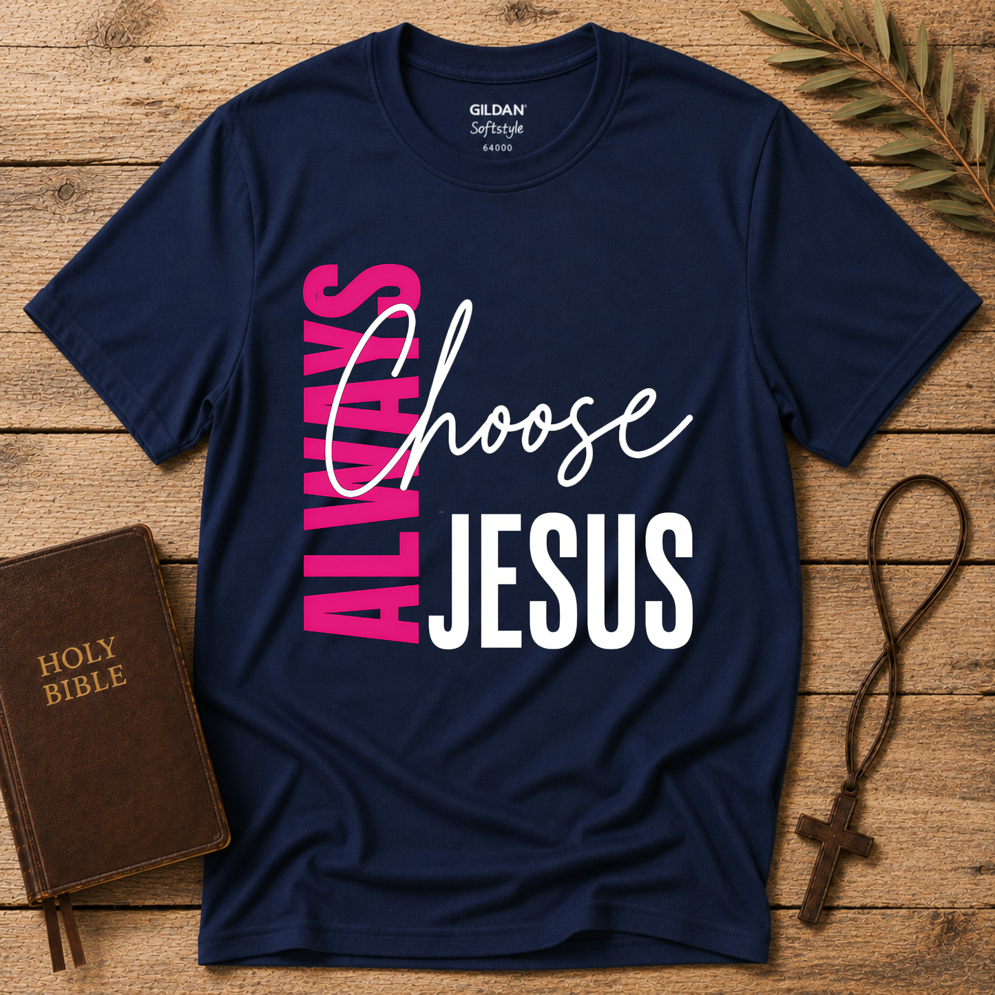 A navy blue GILDAN Softstyle t-shirt with a graphic reading 'ALWAYS Choose JESUS' in pink, white, and black, styled on a rustic wooden background with a Holy Bible, a cross necklace, and a leaf.