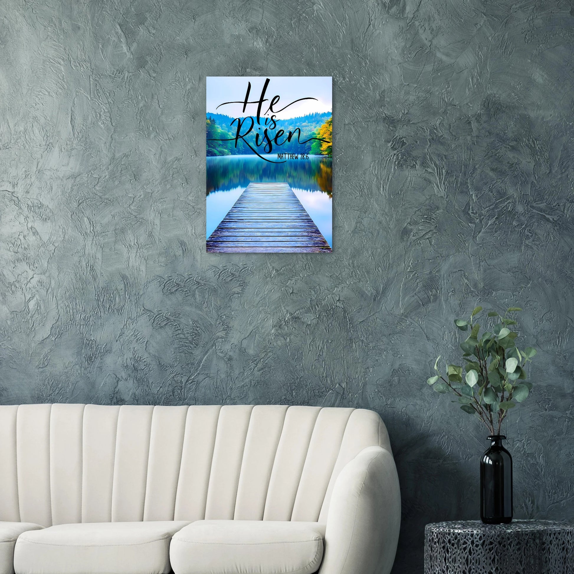 Wall art with 'He is Risen' text over a lake and dock on a textured gray wall.