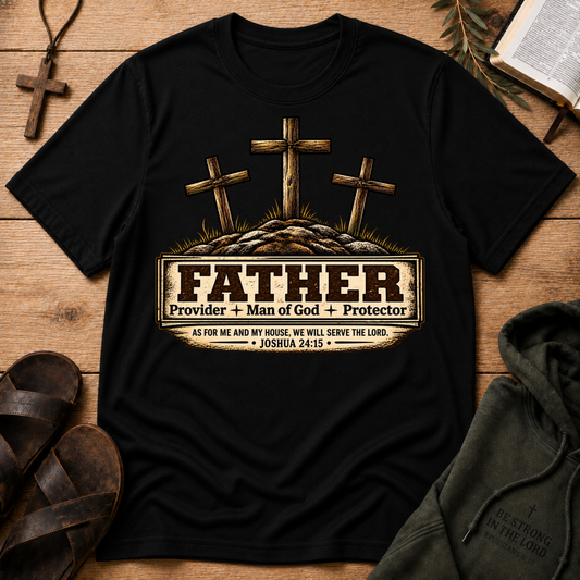 A black short-sleeve graphic T-shirt laid flat on a wooden surface, featuring three crosses above a tombstone-style design with the word 'FATHER' and the phrases 'Provider + Man of God + Protector' and 'AS FOR ME AND MY HOUSE, WE WILL SERVE THE LORD • JOSHUA 24:15'. Surrounding props include a cross, sandals, an open book, and a dark hoodie.