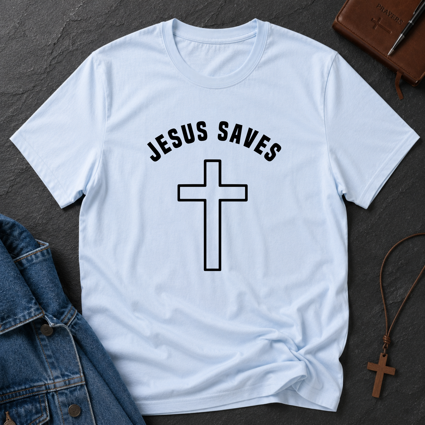 Light blue t-shirt with 'REDEEMED' and cross design on a dark surface with denim jacket and cross necklace.