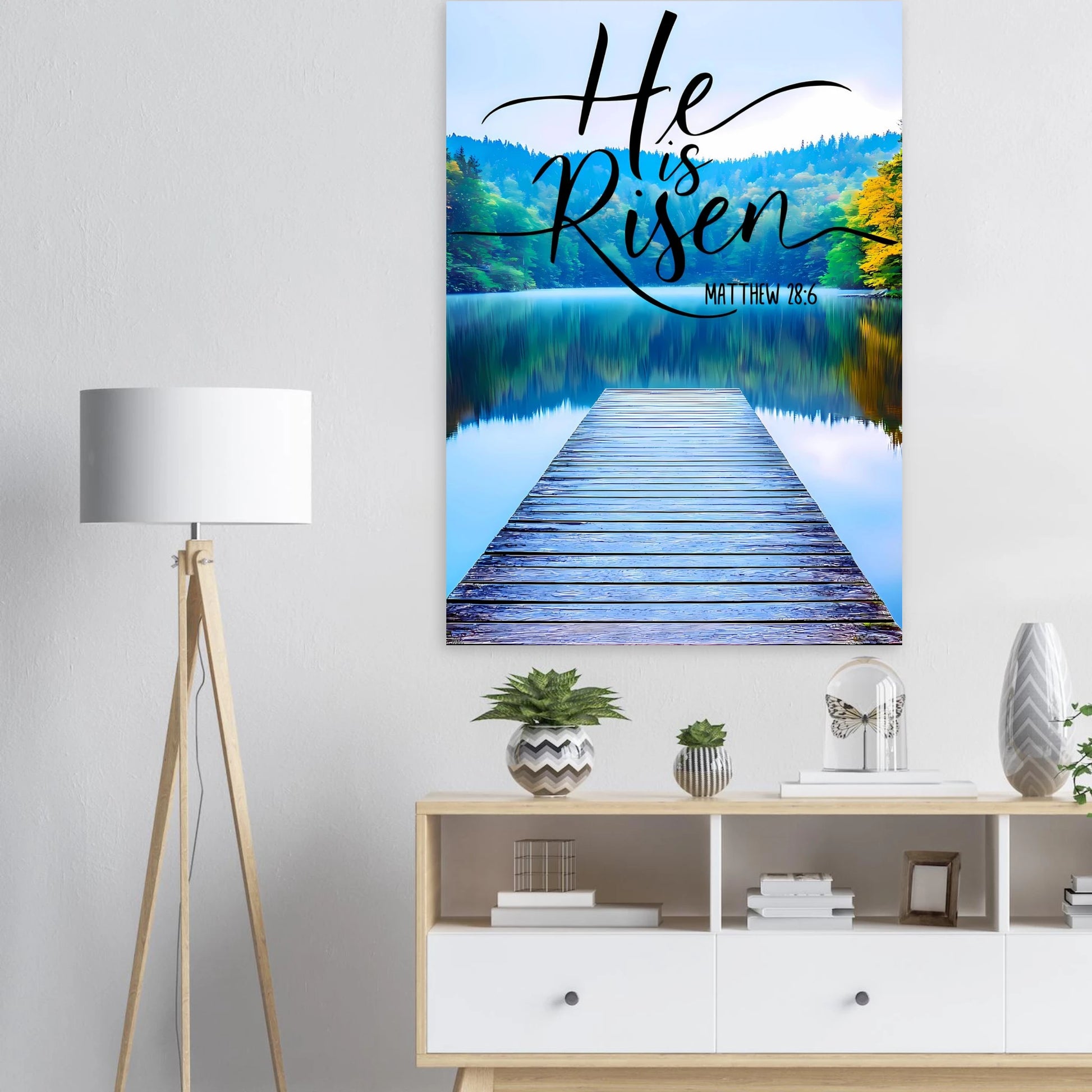 Canvas print with 'He is Risen' text over a lake and dock in a room setting.