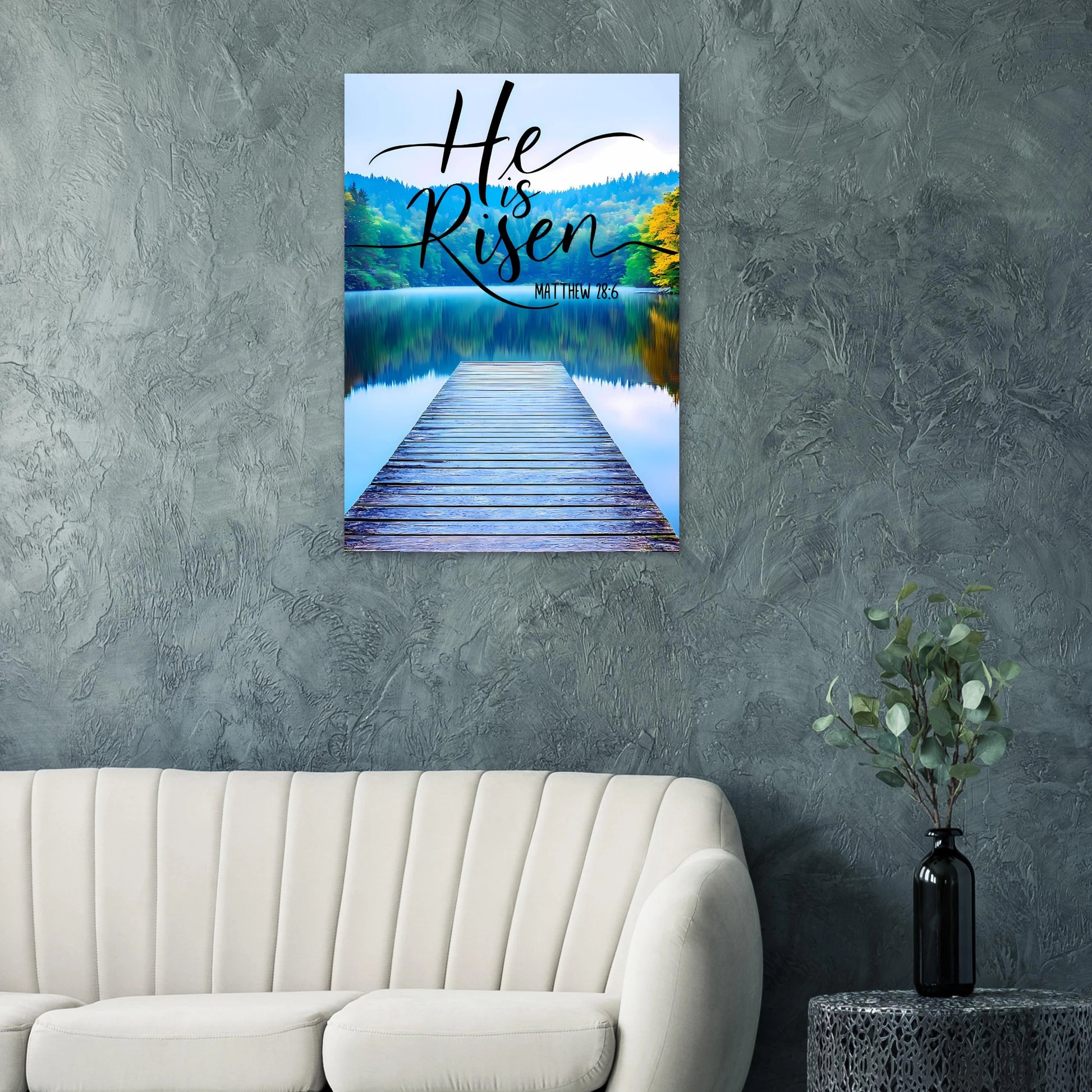Wall art with 'He is Risen' text over a scenic lake and dock, displayed on a gray wall above a sofa.